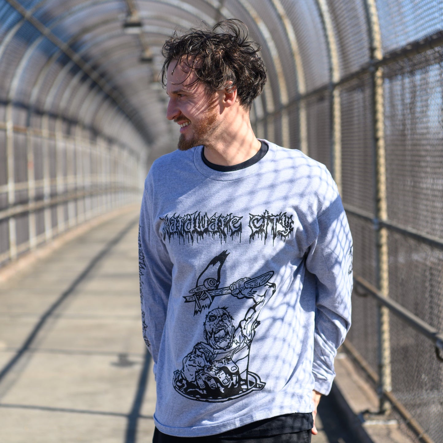 Man wearing a white long-sleeve shirt with black graphics in a metal tunnel on a gray shirt .